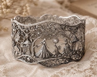 May include: A wide silver cuff bracelet featuring intricate filigree metalwork. The design depicts a detailed scene with figures in long dresses, a castle, trees, and a butterfly. The metal has a polished finish with dark recessed areas.
