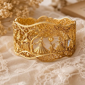 May include: A wide gold cuff bracelet featuring an intricate openwork design. The metal surface depicts two figures in gowns standing among trees, stars, a heart shape, and architectural structures with a scalloped top and bottom edge.