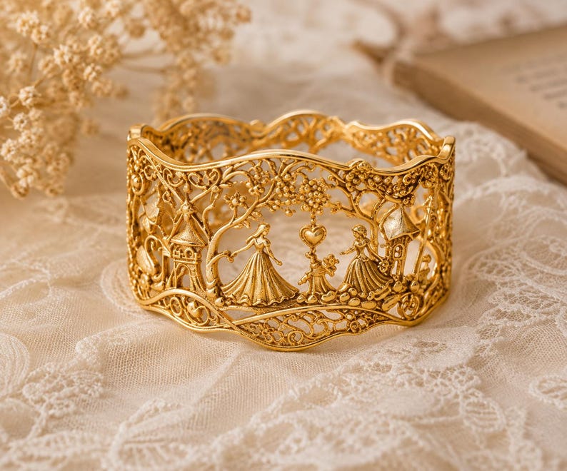 May include: A gold-toned metal cuff bracelet featuring an intricate openwork design. The surface displays a relief scene with two figures in long dresses, a small animal, a heart shape, and architectural structures surrounded by foliage.
