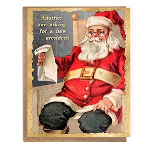 May include: Vintage Christmas card featuring Santa Claus seated in a chair, wearing a red suit and hat, and holding a letter. The card has gold trim and text that reads "Another one asking for a new president."