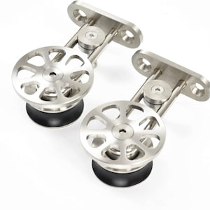 K&ouml;nnte beinhalten: Zwei silberfarbene Schiebet&uuml;rrollen aus Metall mit einem kreisf&ouml;rmigen Raddesign mit acht Aussparungen, einer zentralen Sechskantschraube und einem schwarzen Gummirand. Jede Rolle ist an einer rechteckigen Montageplatte mit zwei Schraubl&ouml;chern befestigt.