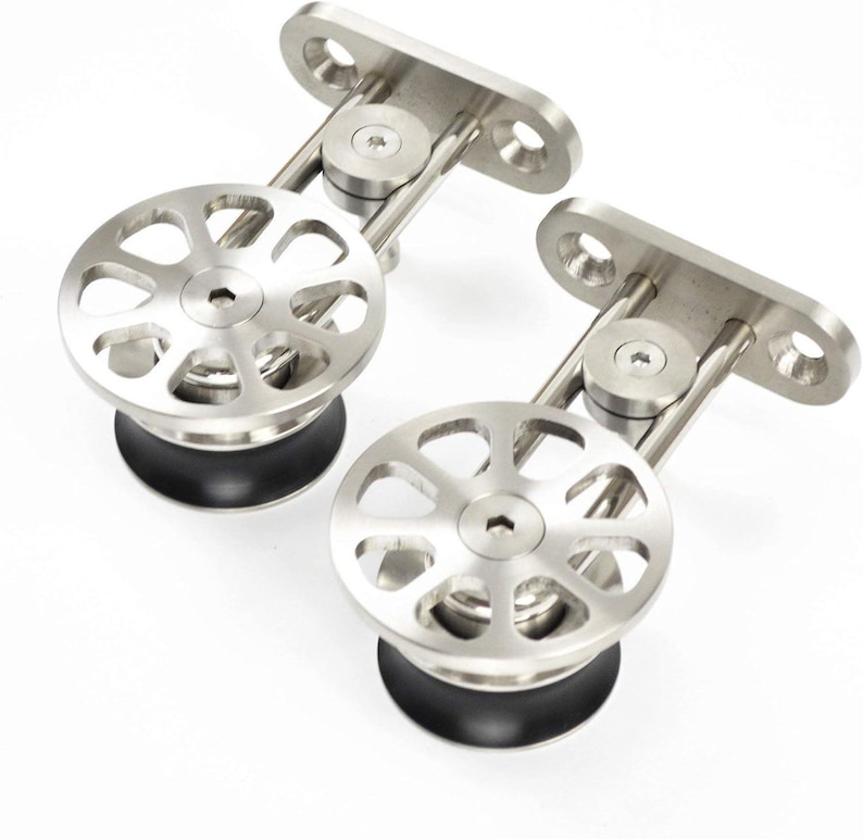 K&ouml;nnte beinhalten: Zwei silberfarbene Schiebet&uuml;rrollen aus Metall mit einem kreisf&ouml;rmigen Raddesign mit acht Aussparungen, einer zentralen Sechskantschraube und einem schwarzen Gummirand. Jede Rolle ist an einer rechteckigen Montageplatte mit zwei Schraubl&ouml;chern befestigt.