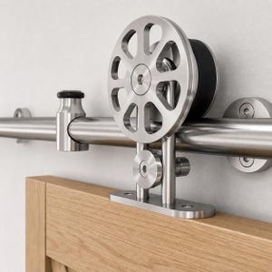 K&ouml;nnte beinhalten: Ein Schiebet&uuml;rbeschlag-Set aus Edelstahl mit einem gro&szlig;en, speichenartigen kreisf&ouml;rmigen Rad mit schwarzem Innenrand. Die Baugruppe umfasst eine horizontale zylindrische Schiene, eine Wandhalterung und eine Metallplatte an einer hellen Holzt&uuml;r.
