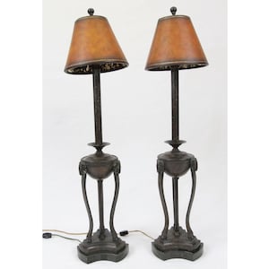 May include: A pair of bronze floor lamps with brown fabric lampshades. The lamps have a classic design with three legs and a round base.