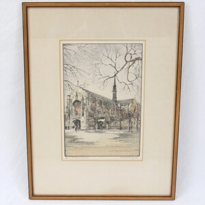 May include: A framed black and white etching of a church building with a tall spire. The building is surrounded by trees and there are people walking in the foreground.