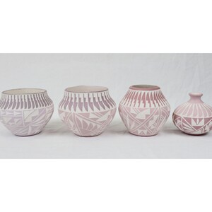 May include: Four ceramic pots with geometric designs in shades of pink and white. The pots vary in size and shape, with the largest two having a rounded form and the smallest being a small vase. The designs include triangles and linear patterns.