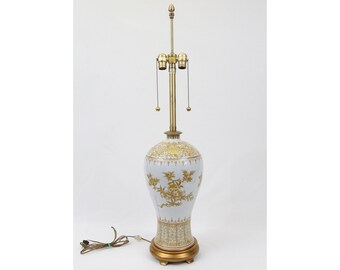 May include: A white porcelain table lamp with gold floral designs. The lamp has a brass base and a finial on top.