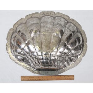 May include: A silver-colored metal shell-shaped mold for baking. The mold is about 12 inches wide and has a textured surface.