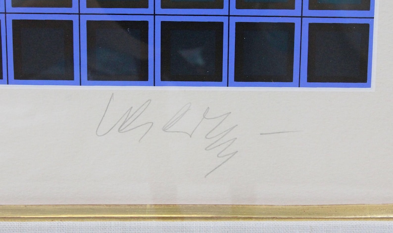May include: Framed artwork featuring a grid of dark squares with blue borders. The artwork has a white border and a gold frame. A signature is visible in the lower center of the artwork.