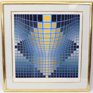 May include: Abstract geometric art print in a gold frame. The artwork features a grid of squares in shades of blue, teal, yellow, and black, creating a three-dimensional effect. The print is mounted on a white mat.