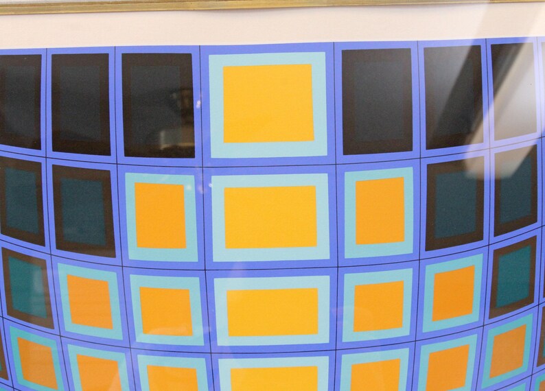 May include: Abstract artwork featuring a grid of squares in a curved pattern. The squares are in shades of black, teal, and orange, outlined in blue and light blue. The artwork is framed in a gold-colored frame.