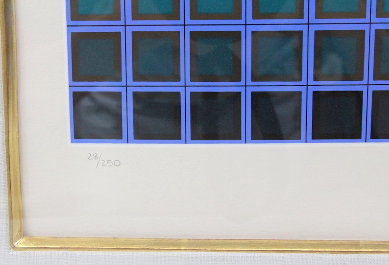May include: Abstract art print featuring a grid of squares in shades of blue, teal, and black, framed in gold. The print is numbered 28/250. The artwork is mounted on a white background.