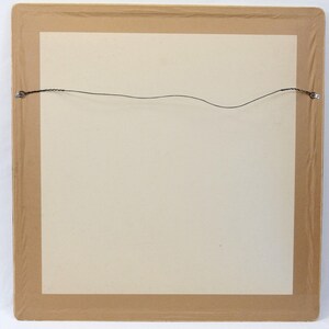 May include: A framed artwork, viewed from the back, with a beige paper and a brown frame. A thin wire is strung across the back for hanging. The frame is sealed with clear plastic.