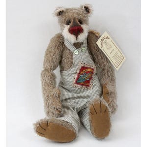 May include: A handmade teddy bear with brown fur, a red nose, and wearing a checkered overall. The bear has a patch on the overall that says "Sweet Corn". A tag that says "teddystyle" is attached to the bear.