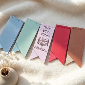 Puede incluir: Cinco marcapáginas de cuero de colores pastel: azul, verde, rosa, rojo y marrón. El marcapáginas rosa tiene el texto "BELIEVE IN YOUR!" y el nombre "Madison". Cada marcapáginas tiene una parte superior cosida y una parte inferior puntiaguda.