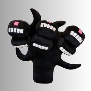 May include: A black plush toy of a multi-headed creature with blocky heads. Each head has a white-toothed grin and a pink square. The toy has a soft, plush texture and a whimsical design, suitable for children.