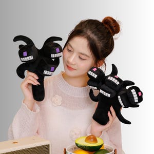 May include: Black plush toy of a three-headed monster with white teeth and purple eyes. The toy has a long handle and is designed to resemble a character from a popular video game. The plush toy is soft and cuddly.
