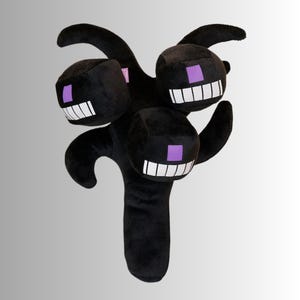 May include: A black plush toy with a multi-headed design and a central stem. Each head has a white-toothed grin and a purple square eye. The toy has curved arms and is designed to resemble a Minecraft Wither.