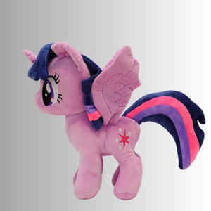 Könnte beinhalten: Ein Plüschpferd in Rosa, Lila und Blau mit Horn, Flügeln und einem mehrfarbigen Schweif. Das Pony hat ein Sternen-Emblem an der Flanke und große, ausdrucksstarke Augen.