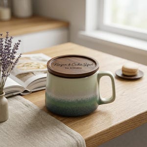 May include: A ceramic mug with a green and white gradient finish and a handle, topped with a circular wooden lid. The lid is engraved with the text Keagan & Caden Sifert and Est. 8/29/2026 in a dark script and sans-serif font combination.