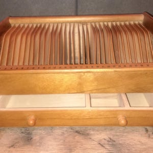 May include: A wooden desk organizer with a series of vertical dividers and a pull-out drawer with three compartments. The organizer has a light brown finish and a ruler along the top edge.
