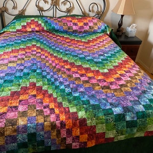 May include: A colorful quilt with a patchwork design in shades of green, purple, brown, and orange. The quilt is made with a variety of fabrics and has a quilted pattern.