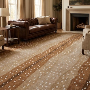 May include: A large area rug with a deer-inspired pattern in shades of brown and beige. The rug features a repeating pattern of brown stripes with white dot accents, creating a natural, organic design. The rug is placed in a living room setting with a leather sofa and fireplace.