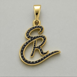 May include: A gold pendant in the shape of the cursive letters SR, featuring a polished gold finish and a pavé setting of small, round, black stones that follow the curves of the letters, complete with a gold bail at the top for a chain.