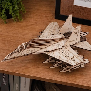 May include: A wooden model of a fighter jet, featuring intricate laser-cut details. The model is light brown and has the text "CV-30" and Cyrillic text on the wings. The model is displayed on a wooden shelf.
