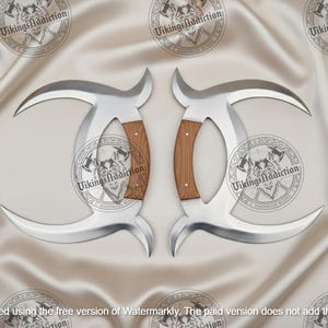 May include: Two silver-colored, curved blades with wooden handles. The blades have a crescent shape and are displayed on a satin-like surface. The handles are a light brown color. The text "VikingsAddiction" is visible.