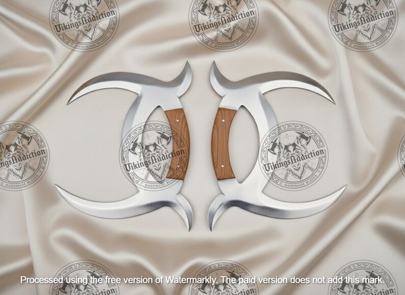 May include: Two silver-colored, curved blades with wooden handles. The blades have a crescent shape and are displayed on a satin-like surface. The handles are a light brown color. The text "VikingsAddiction" is visible.