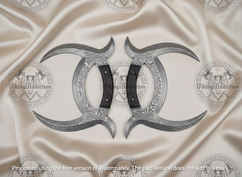 May include: Two curved, Damascus steel blades with black handles. The blades have a unique pattern and are arranged symmetrically. The background is a light-colored, textured fabric. The text "VikingsAddiction" is visible.