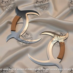 May include: Two curved, silver-colored blades with wooden handles are displayed on a satin surface. The blades have a unique, crescent-like shape with a dark, curved top. The handles are a light brown color. The image has a watermark that says "Vikings Addiction".