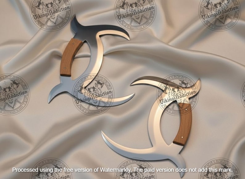 May include: Two curved, silver-colored blades with wooden handles are displayed on a satin surface. The blades have a unique, crescent-like shape with a dark, curved top. The handles are a light brown color. The image has a watermark that says "Vikings Addiction".