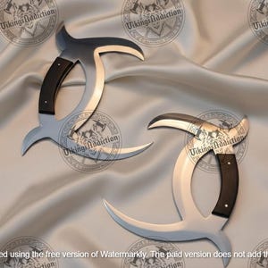 May include: Two silver-colored, curved knives with black handles are displayed on a satin surface. The blades have a unique, crescent-like shape. The handles are dark, and the overall design suggests a historical or fantasy theme.