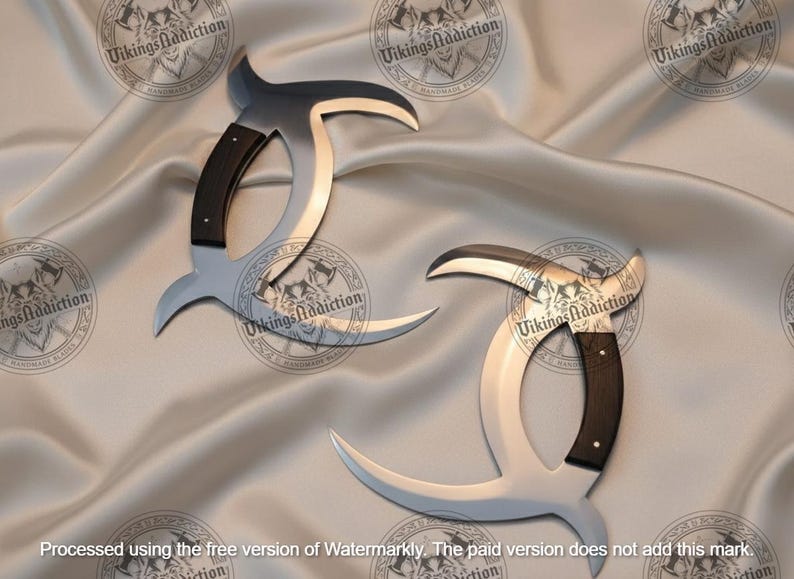 May include: Two silver-colored, curved knives with black handles are displayed on a satin surface. The blades have a unique, crescent-like shape. The handles are dark, and the overall design suggests a historical or fantasy theme.