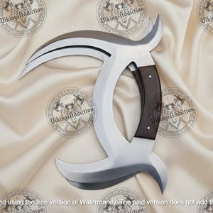 May include: A large, curved blade with a polished steel finish and a dark wood handle. The blade has a unique, crescent-like shape with a sharp edge. The handle is riveted and ergonomically designed. The blade is displayed on a cream-colored satin fabric.
