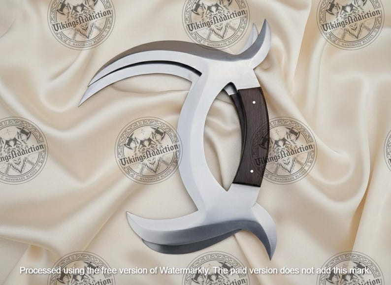 May include: A large, curved blade with a polished steel finish and a dark wood handle. The blade has a unique, crescent-like shape with a sharp edge. The handle is riveted and ergonomically designed. The blade is displayed on a cream-colored satin fabric.