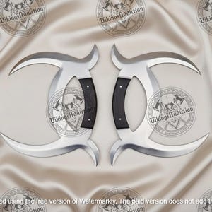 May include: Two silver-colored, curved blades with black handles. The blades have a crescent shape and are displayed on a cream-colored, satin-like surface. The handles are dark with a textured appearance.