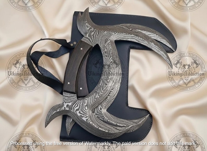 May include: A Damascus steel karambit knife with a dark wooden handle and a black leather sheath. The blade has a unique curved design. The knife is displayed on a cream-colored fabric.