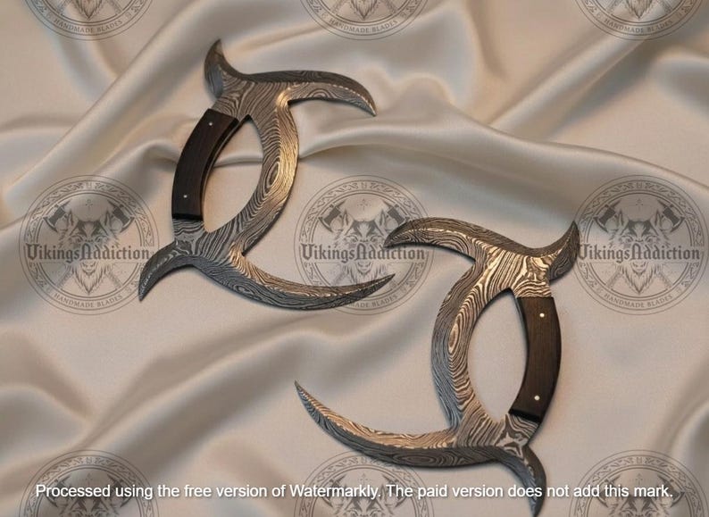 May include: Two Damascus steel karambit knives with curved blades and dark wood handles. The blades have a unique pattern, and the handles are riveted. The knives are displayed on a satin fabric.