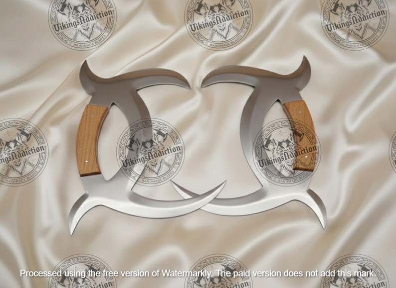 May include: Two silver-colored, curved blades with wooden handles. The blades have a unique shape with a pointed tip and a curved top. The handles are made of light brown wood. The background is a white, silky fabric with circular logos.