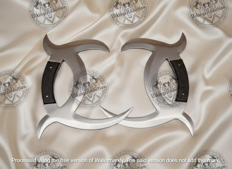 May include: Two silver-colored, curved blades with black wooden handles. The blades have a unique shape with a hook at the top and a pointed end. The blades are displayed on a white, textured surface.