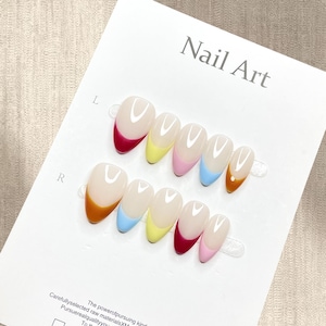 Puede incluir: Un juego de uñas artificiales con base transparente y puntas de colores. Las puntas están pintadas en rojo, amarillo, rosa, azul y naranja. Las palabras "Nail Art" están impresas en gris sobre la tarjeta blanca.