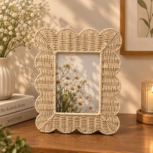 Op de afbeelding: Een rechthoekige fotolijst van lichtbeige gevlochten rotan met een geschulpte rand. De lijst bevat een foto van witte, margrietachtige bloemen met gele harten, geplaatst tegen een zachte, neutraal gekleurde achtergrond.