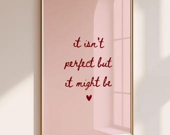 May include: A rectangular wall art print in a thin gold frame featuring a light pink background with dark red cursive text that reads: it isn't perfect but it might be, followed by a small dark red heart symbol centered at the bottom.