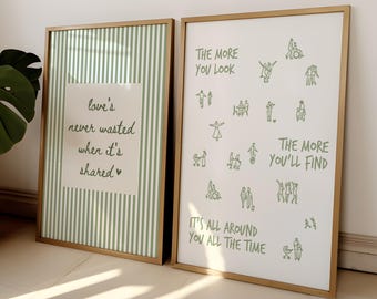 May include: Two framed wall art prints with gold frames. The left print has green and white vertical stripes with the text "love's never wasted when it's shared". The right print features green line drawings of people and the text "THE MORE YOU LOOK THE MORE YOU'LL FIND IT'S ALL AROUND YOU ALL THE TIME".