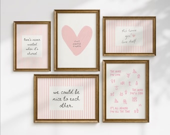 May include: A gallery wall set of five framed prints with gold frames. The prints feature pink and white vertical stripes, a pink heart, and text including 'love's never wasted when it's shared', 'it isn't perfect but it might be', and 'we could be nice to each other'.