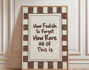 May include: A rectangular framed wall art piece featuring a cream-colored center with the dark brown text: How Foolish To Forget How Rare All Of This is. The border consists of a repeating pattern of dark brown and cream-colored blocks.