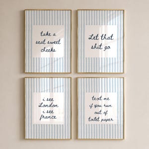 May include: A set of four rectangular wall art prints in thin gold frames. Each print features a light blue and white vertical striped border with a white center containing dark blue text: take a seat sweet cheeks, Let that shit go, i see London i see france, and text me if you run out of toilet paper.